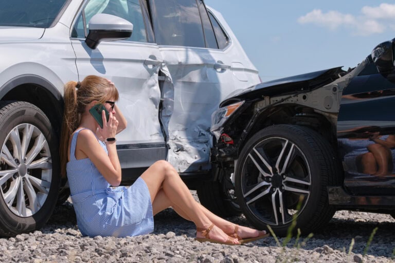 Stressed woman driver talking on mobile phone on street side calling for emergency service after car accident.